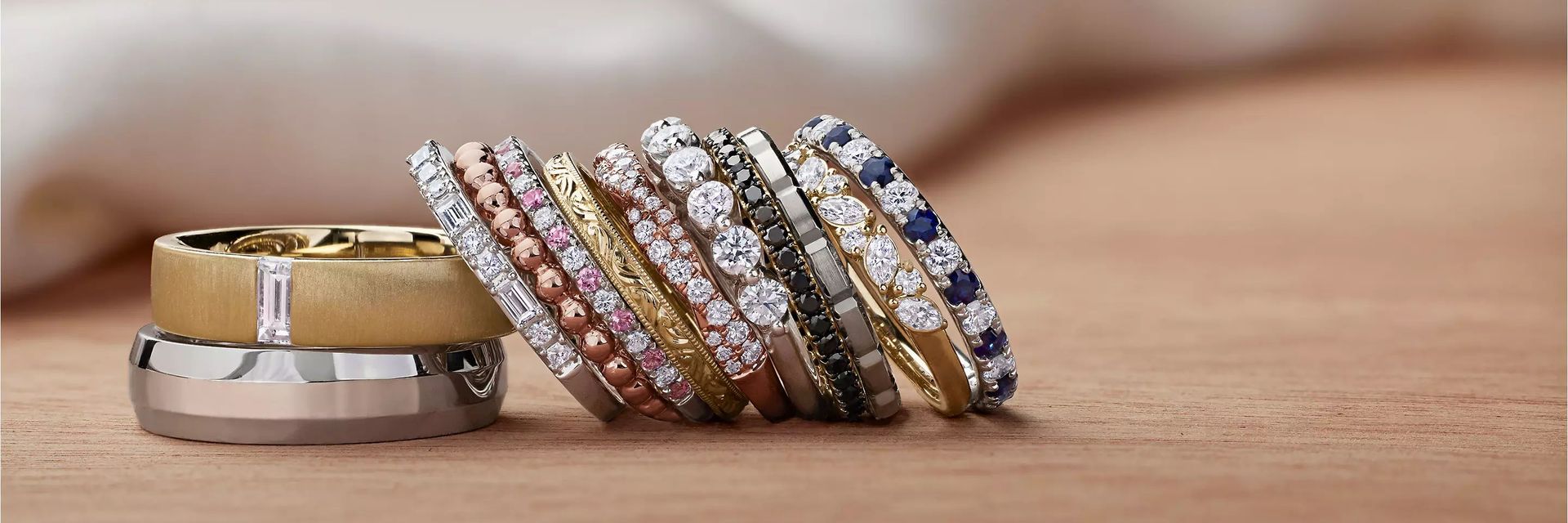 12 wedding rings with a variety of diamonds, metals, and designs, all on a beige surface